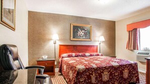 Habitación de hotel con cama, escritorio, silla, mesita de noche, dos lámparas de pared y un cuadro en la pared.