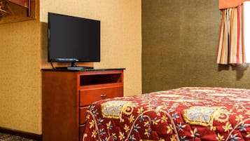 A hotel room with a bed, a television on a wooden dresser, and a patterned bedspread.