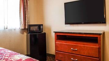 A hotel room with a bed, a TV mounted on the wall, a microwave, and a wooden dresser with drawers.