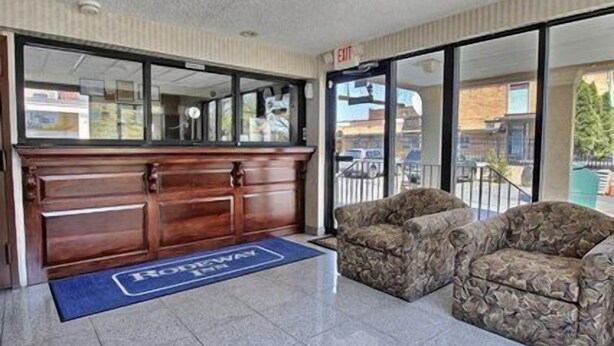 Un área de recepción con un escritorio de madera, dos sillones estampados y un tapete azul con el nombre del hotel.