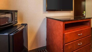 Habitación de hotel compacta con microondas, refrigerador pequeño, cómoda de madera con cajones y televisor de pantalla plana montado.