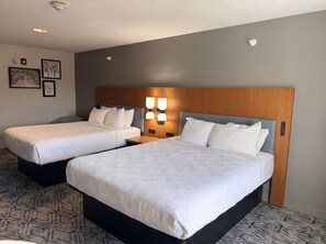 Habitació d'hotel amb dos llits, un panell de fusta al capçal, una làmpada penjada a la paret i quadres emmarcats.