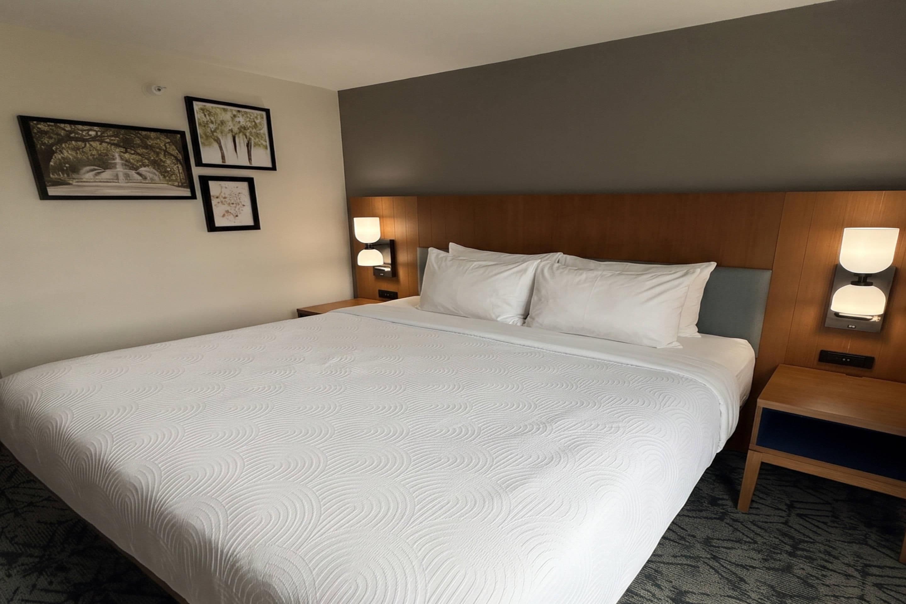 Ein Hotelzimmer mit einem großen Bett, zwei Nachttischen mit Lampen und gerahmten Bildern an der Wand.