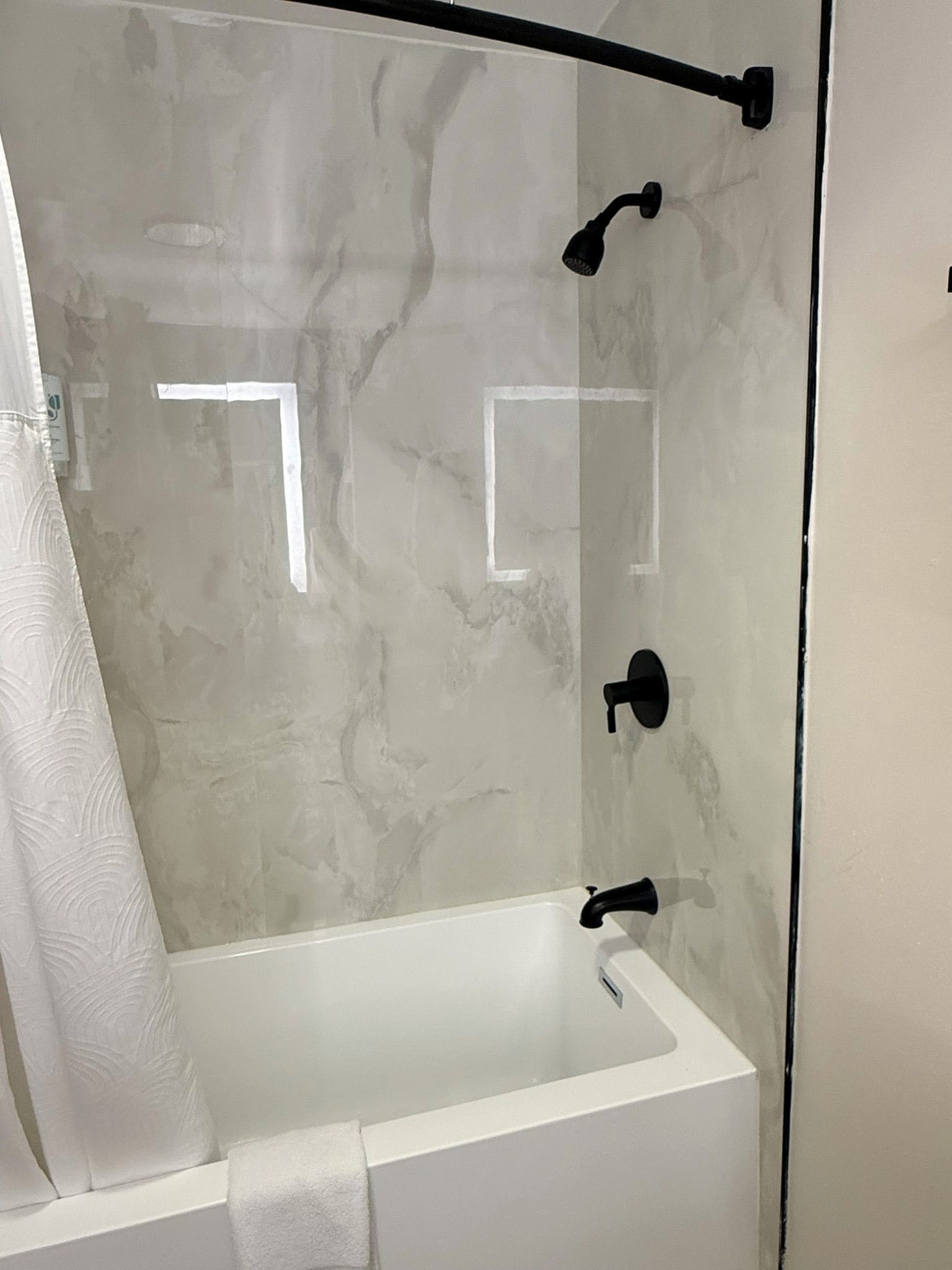 Una ducha con cerramiento de vidrio, una bañera blanca, un perchero y un cabezal de ducha.