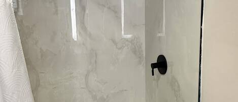 Una ducha con cerramiento de vidrio, una bañera blanca, un perchero y un cabezal de ducha.