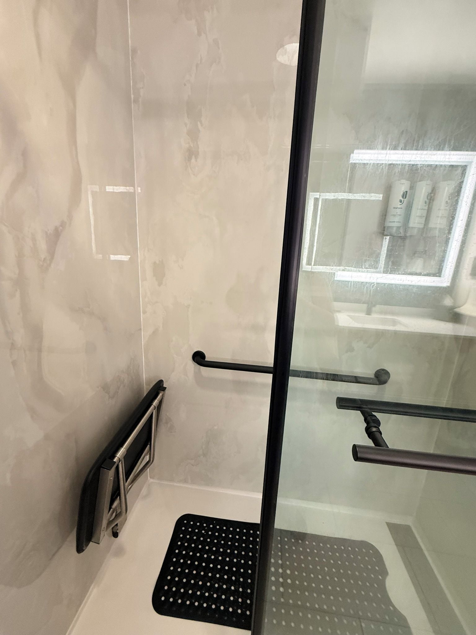 A bathroom with a glass shower enclosure, a black grab bar, and a white tiled floor.
