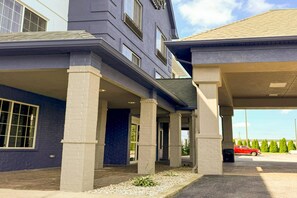 A hotel with a covered outdoor area, multiple windows, and a red car parked outside.