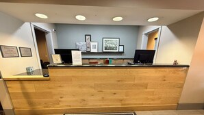 A reception desk with a 'WELCOME' mat, framed pictures on the wall, and a check-in/out schedule. - Country Inn & Suites by Radisson, Lima (Lima)