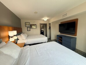 Habitación de hotel con dos camas, televisión, escritorio y armario.