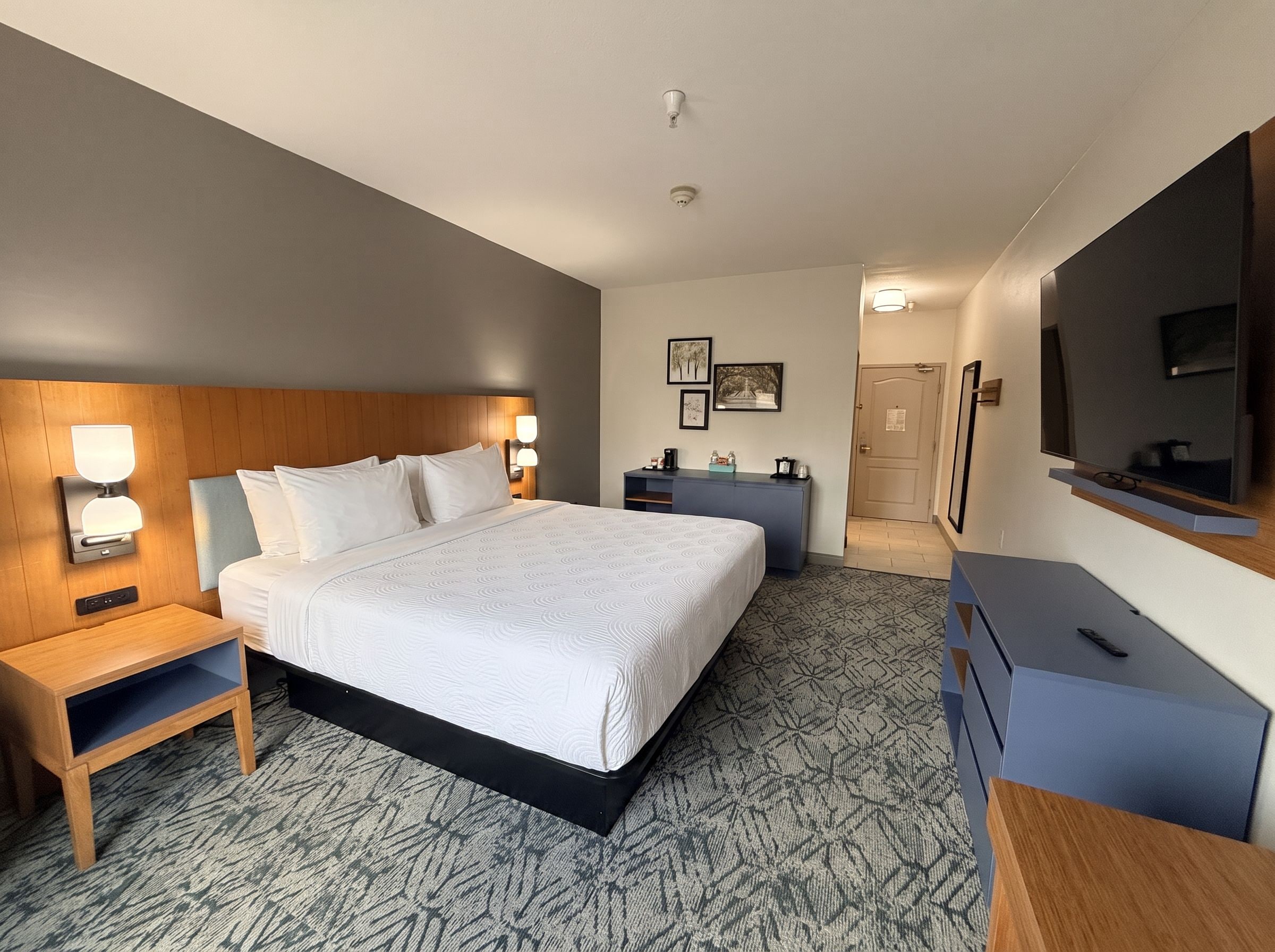 A hotel room with a large bed, bedside tables, a dresser, a television, and a door leading to a bathroom.
