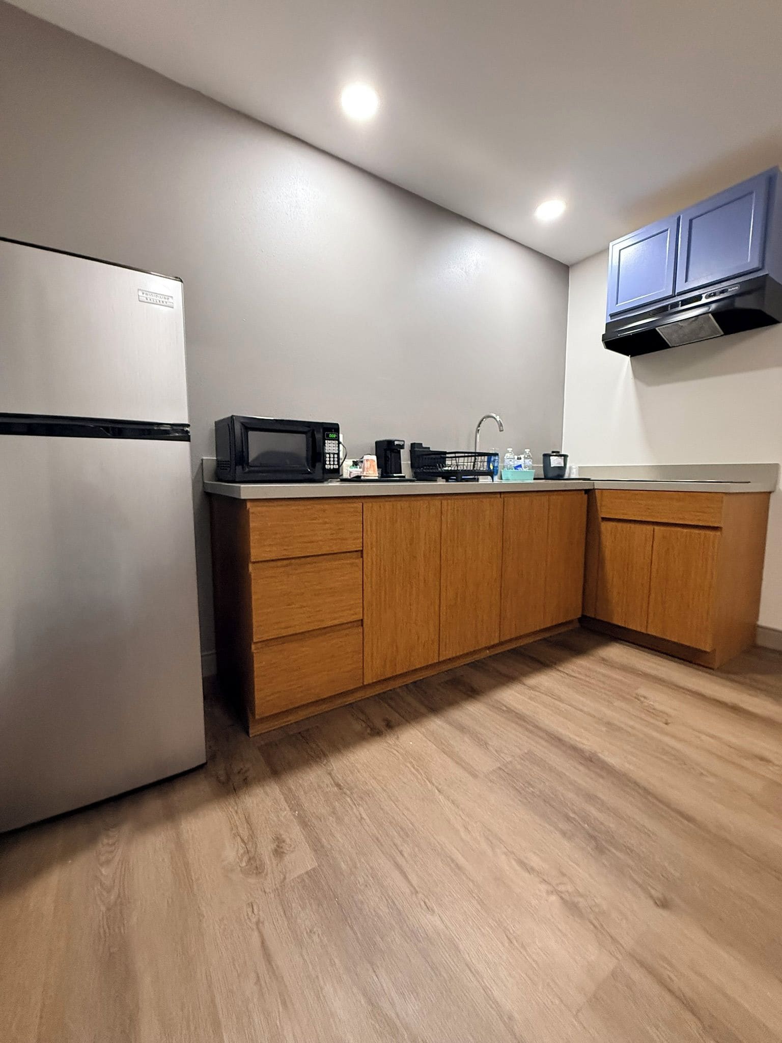 Una cocina con refrigerador, microondas, cafetera y gabinetes de madera.