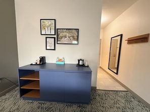 A reception desk with a coffee maker, a water bottle, and a small plant. There are three framed pictures on the wall above the desk. - Country Inn & Suites by Radisson, Lima (Lima)