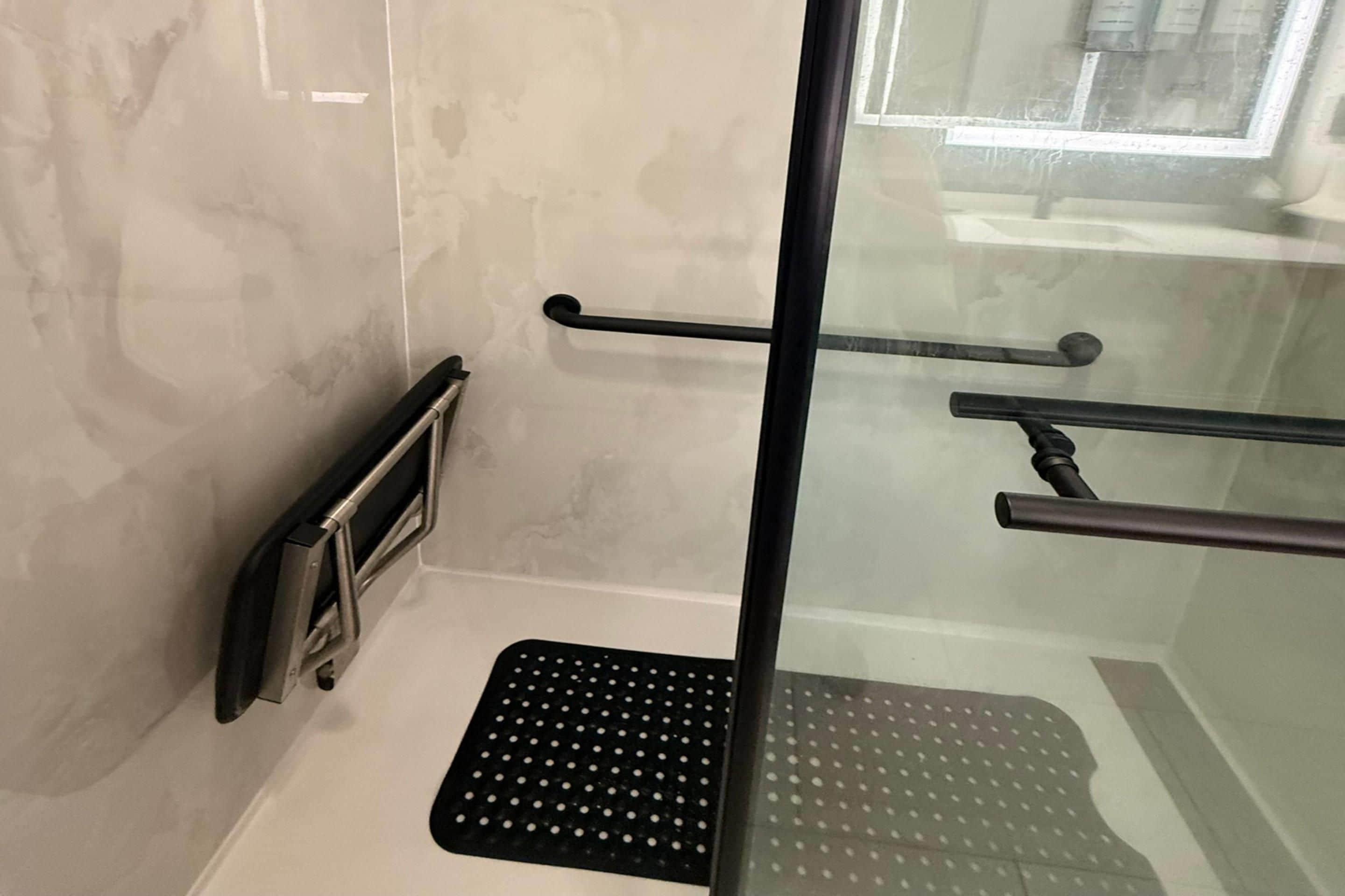 A bathroom with a glass shower enclosure, a black non-slip mat, and a towel rack.