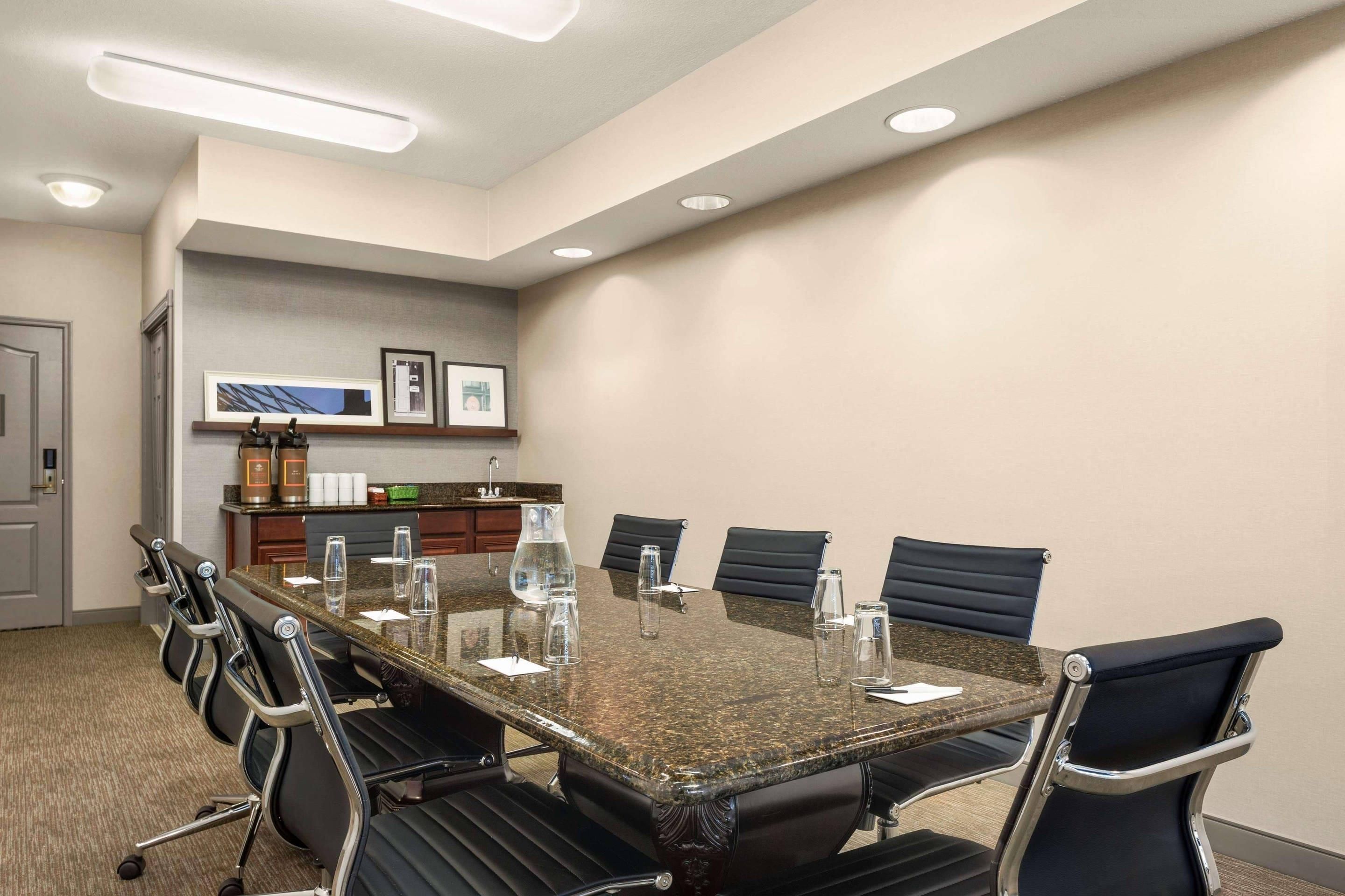 A conference room with a large table, chairs, and a kitchenette area.