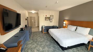 A hotel room with a bed, a desk with a flat-screen TV, a sofa, and a wall-mounted TV.