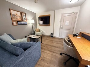 Ett rum med en blå soffa, ett litet bord, en lampa, en stol, ett skrivbord och en dörr.