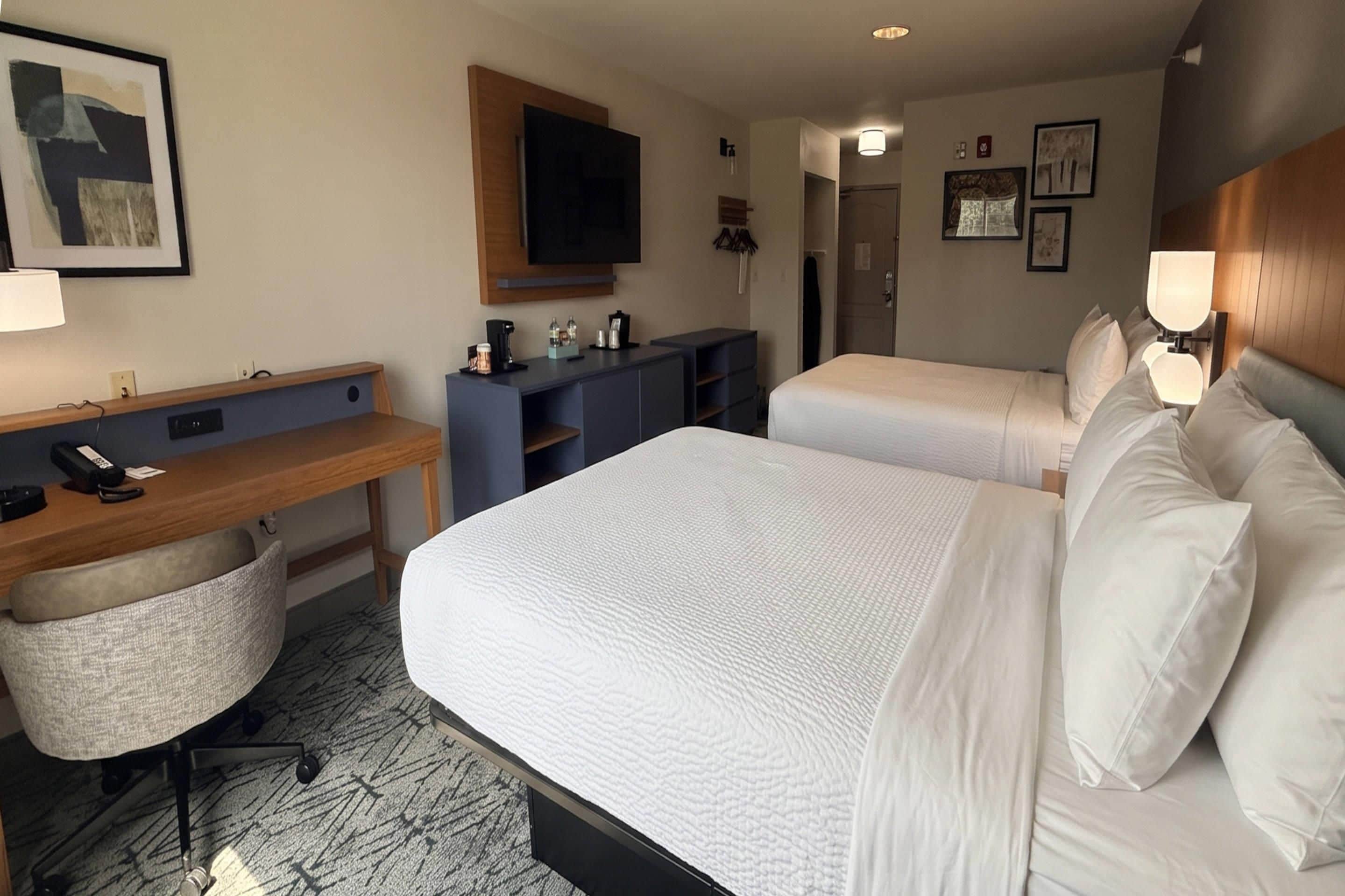 A hotel room with a bed, a desk, a chair, a TV, and a wardrobe.