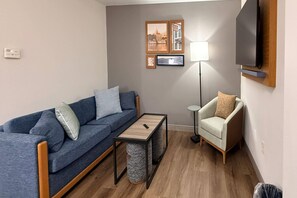 A living room with a blue sofa, a small coffee table, a lamp, a TV, and a chair. - Country Inn & Suites by Radisson, Lima (Lima)