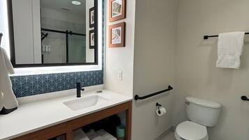 Un baño moderno con un espejo grande, un lavamanos blanco y un inodoro. Hay cuadros en la pared y un perchero para toallas.