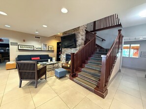 A spacious living area with a staircase, a flat-screen TV mounted on a stone wall, and a sofa with a red cushion. - Country Inn & Suites by Radisson, Lima (Lima)