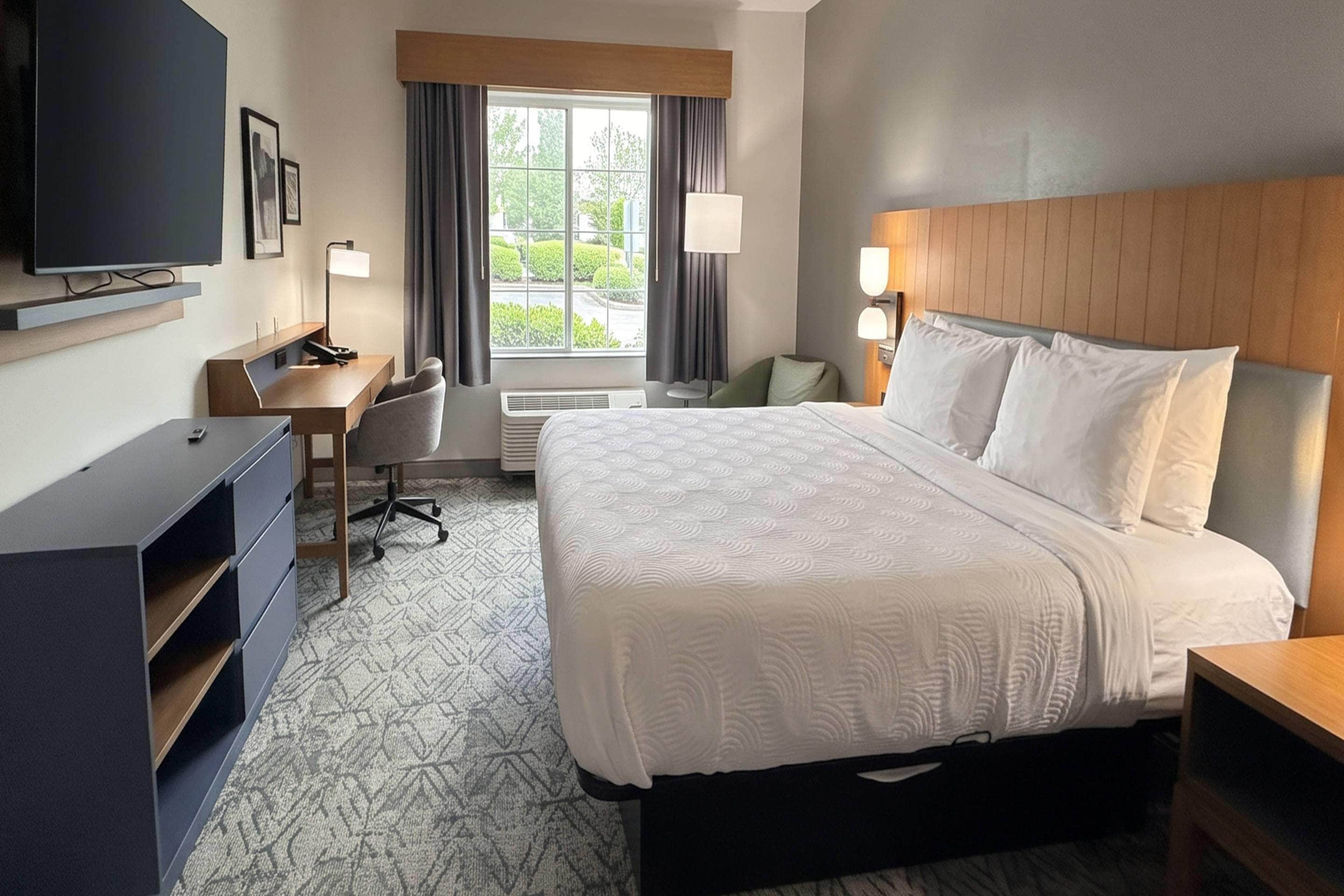 A hotel room with a bed, desk, chair, TV, and a window with curtains.