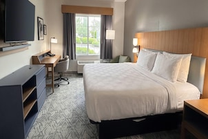 Habitación de hotel con cama, escritorio, silla, televisor y ventana con cortinas.
