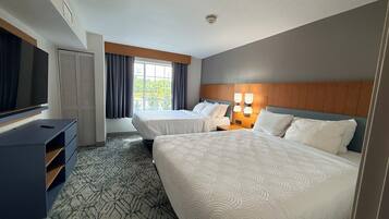 A hotel room with two beds, a television, a desk, and a window with curtains.
