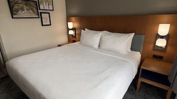 Quarto de hotel com uma cama grande, duas mesas de cabeceira e luminárias fixadas na parede.