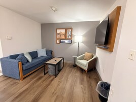 Een woonkamer met een bank, fauteuil, salontafel en een aan de muur bevestigde televisie.