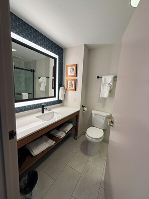 A bathroom with a large mirror, two sinks, a toilet, and a towel rack.