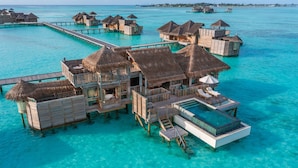 Een bungalow op het water met rieten daken, een privézwembad en een houten terras.