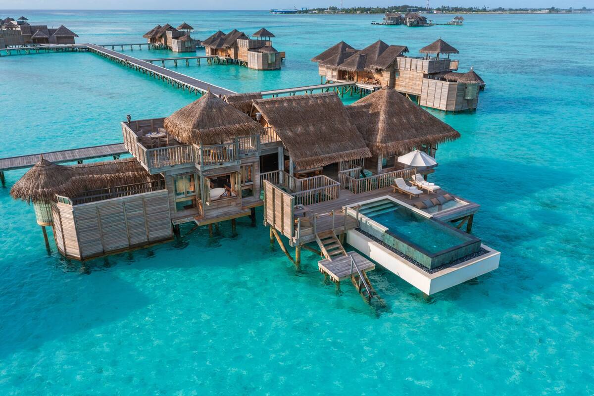 Ein Bungalow auf Stelzen mit Reetdach, einem privaten Pool und einer Holzterrasse.