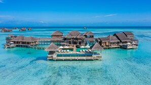 Bungalows op het water met rieten daken, helder turquoise water en een houten terras.