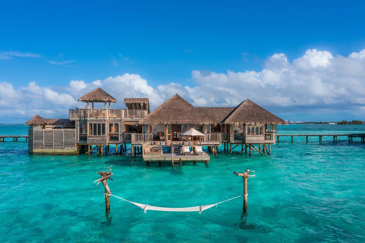 Ein luxuriöses Bungalow auf Stelzen mit Strohdach, Holzterrasse und klarem türkisblauem Wasser.