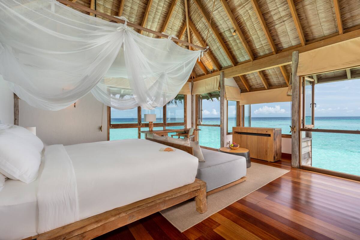Ein geräumiges Schlafzimmer mit einem großen Bett, einer hölzernen Sitzbank und Meerblick.
