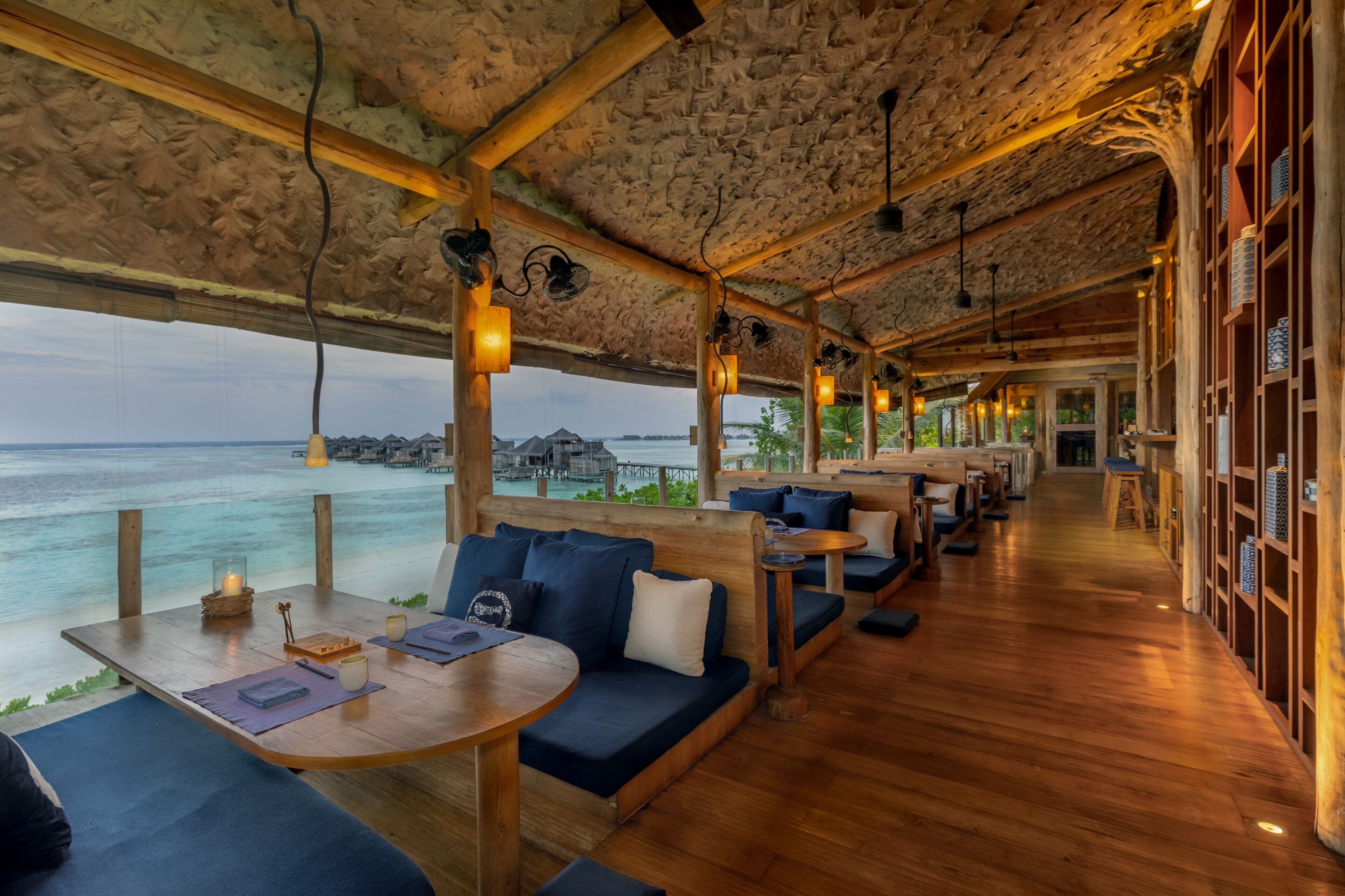 Interior de madera con asientos y mesas, con vistas a un cuerpo de agua.