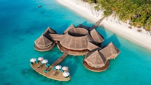 Overwater bungalows met rieten daken, houten looppaden en loungegedeeltes met parasols.