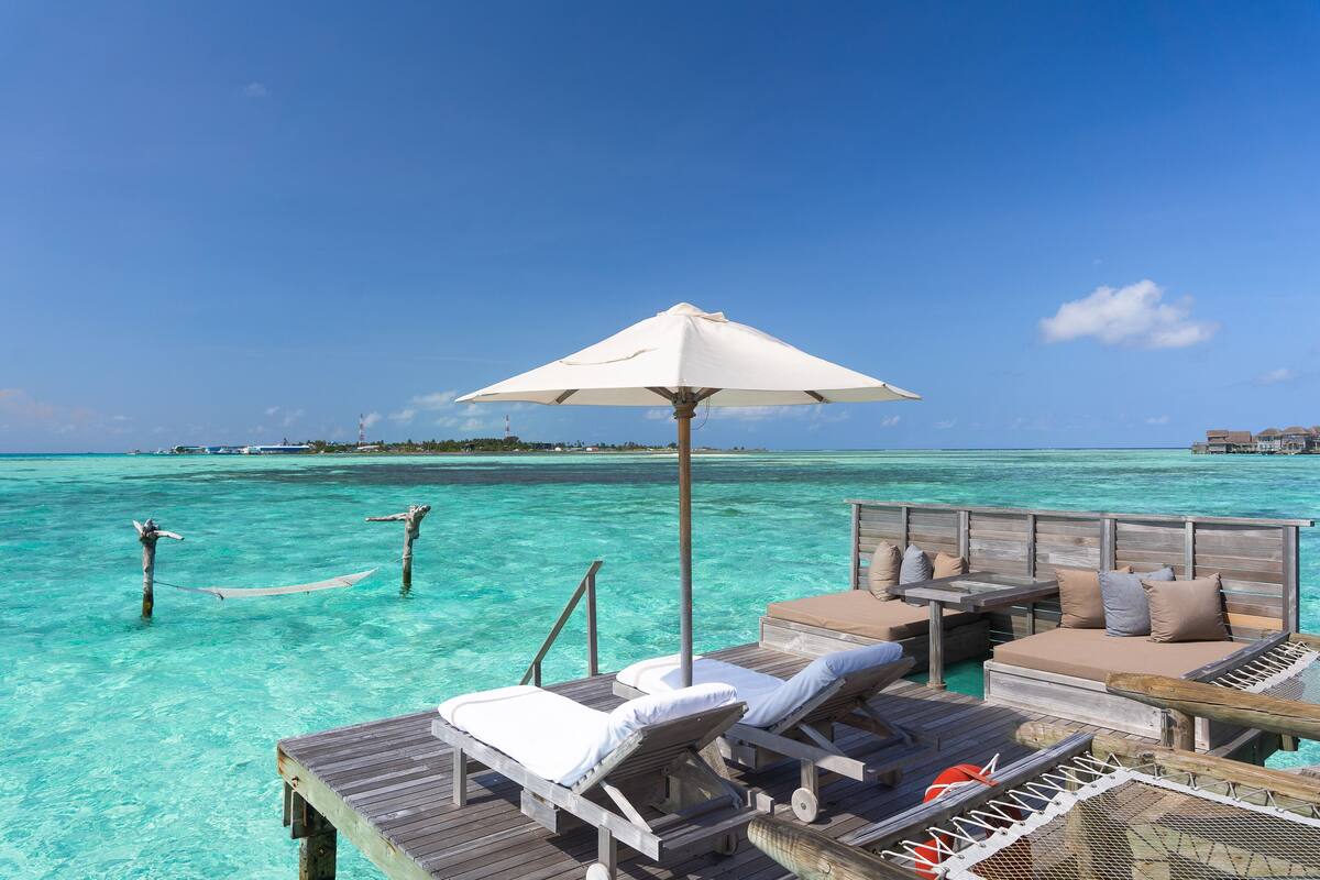 Eine Holzterrasse mit Liegestühlen und einem Tisch, mit Blick auf türkisfarbenes Wasser und entfernte Inseln.