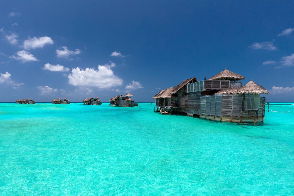 Wasserbungalows mit Strohdächern, klares türkisblaues Wasser und einem strahlend blauen Himmel.