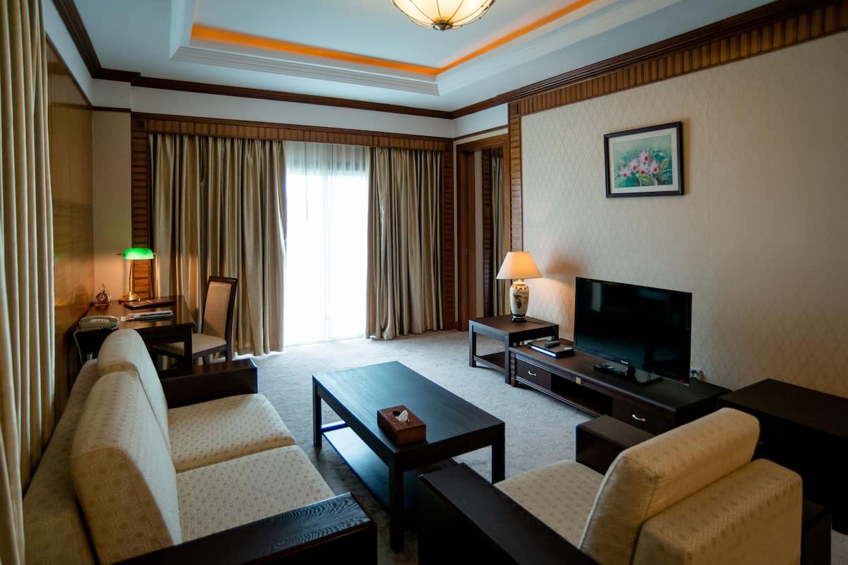 Quarto de hotel com sofá, mesa de centro, televisão, luminária e um quadro na parede.