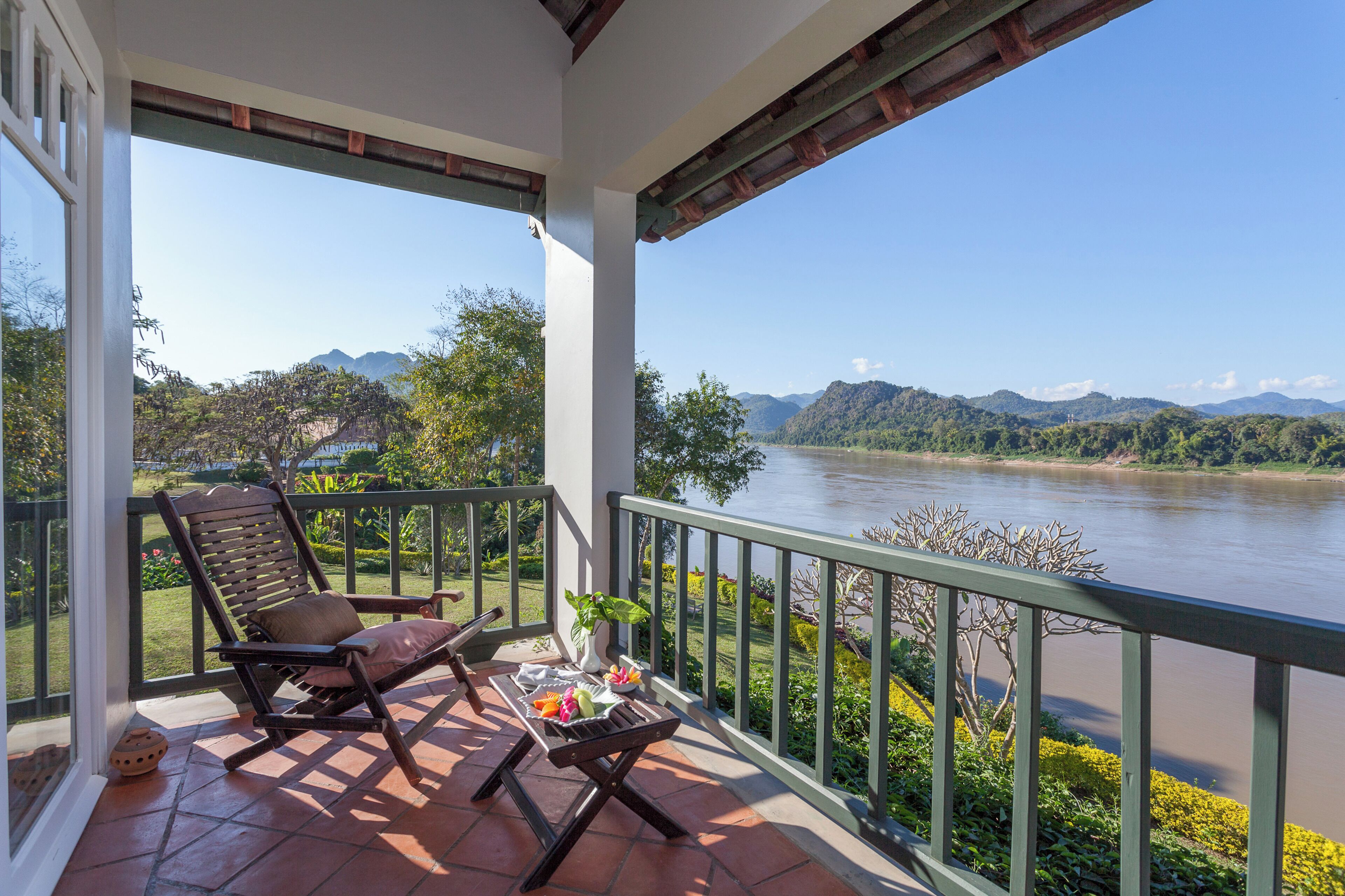 Un balcon avec vue sur une rivière et des montagnes, un barbecue avec de la nourriture et une chaise.