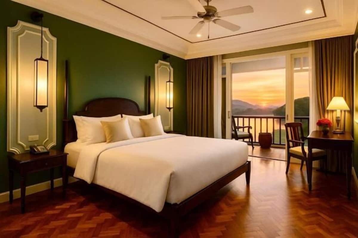 Ein Hotelzimmer mit Bett, Nachttisch, Schreibtisch mit Stuhl, Balkon und Deckenventilator.