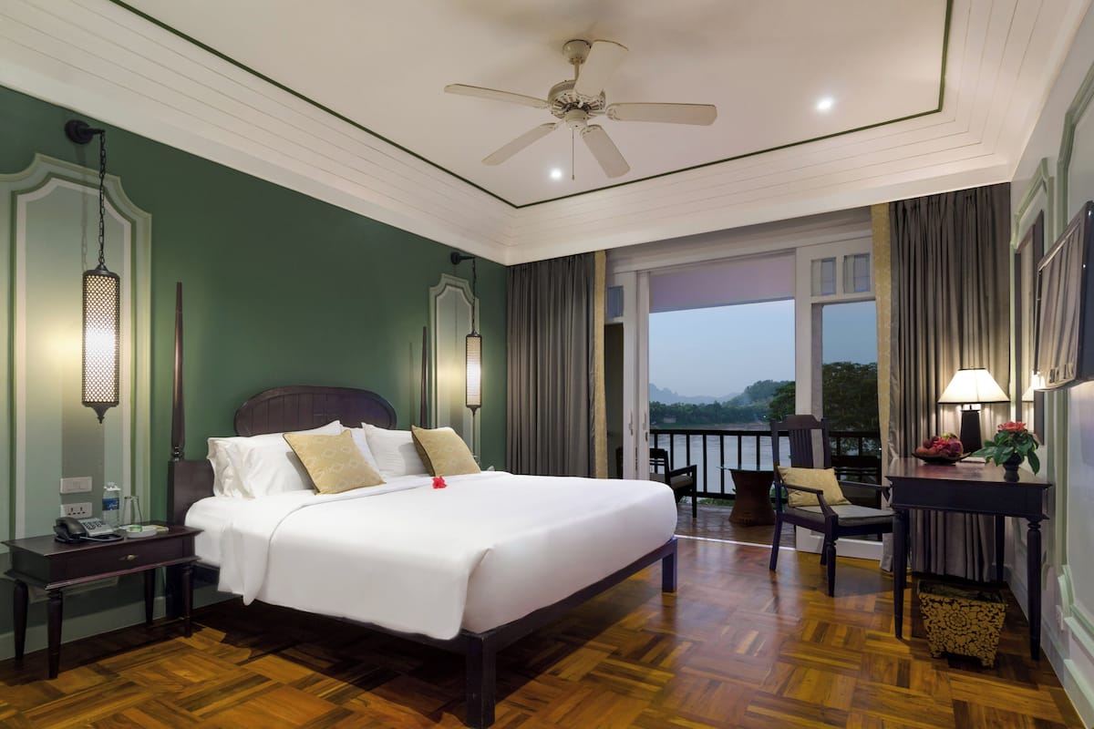 Ein Hotelzimmer mit einem großen Bett, einem Schreibtisch, einem Stuhl, einem Balkon mit Blick und einem Deckenventilator.
