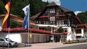 Un bâtiment traditionnel à colombages, doté d’un balcon, entouré de fleurs rouges et orné d’un drapeau.