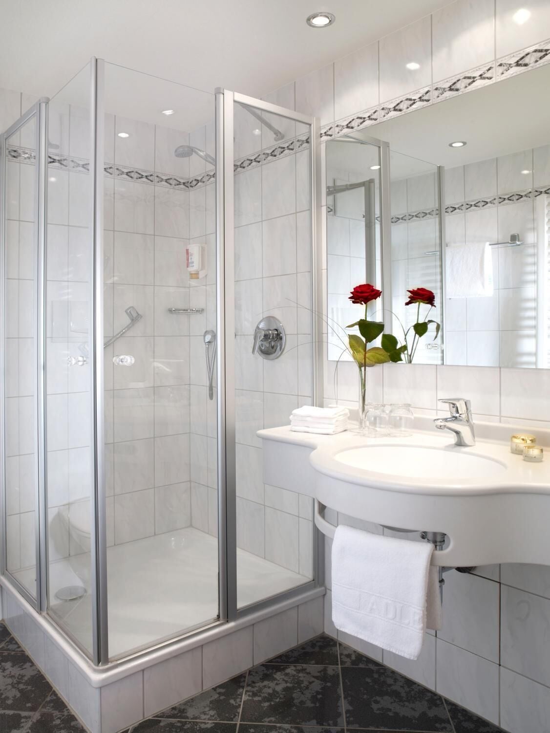 A modern bathroom with a glass-enclosed shower, a white sink with a mirror, and a towel rack.