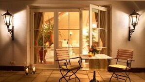 Un espace patio accueillant avec une table et deux chaises, une plante en pot et une vue, à travers une porte vitrée, sur un intérieur bien éclairé.