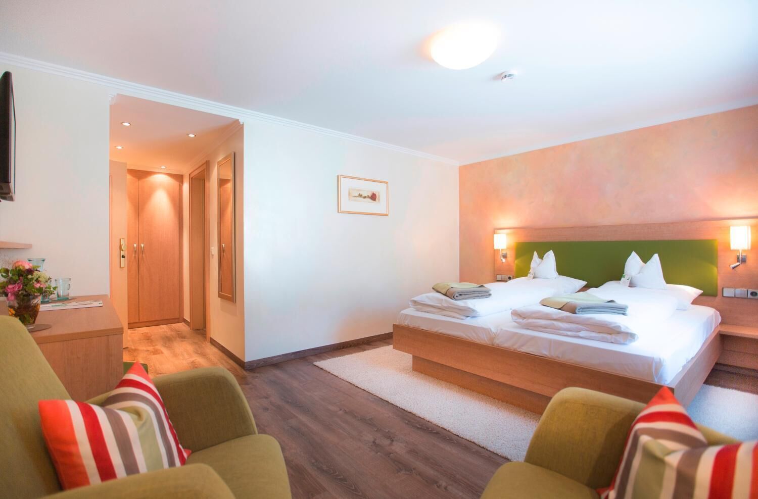 Habitación de hotel con cama, escritorio, silla y una mesita con un florero.