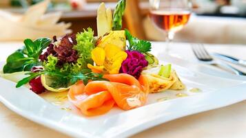 Een vierkant wit bord met een salade, zalm en een glas wijn.