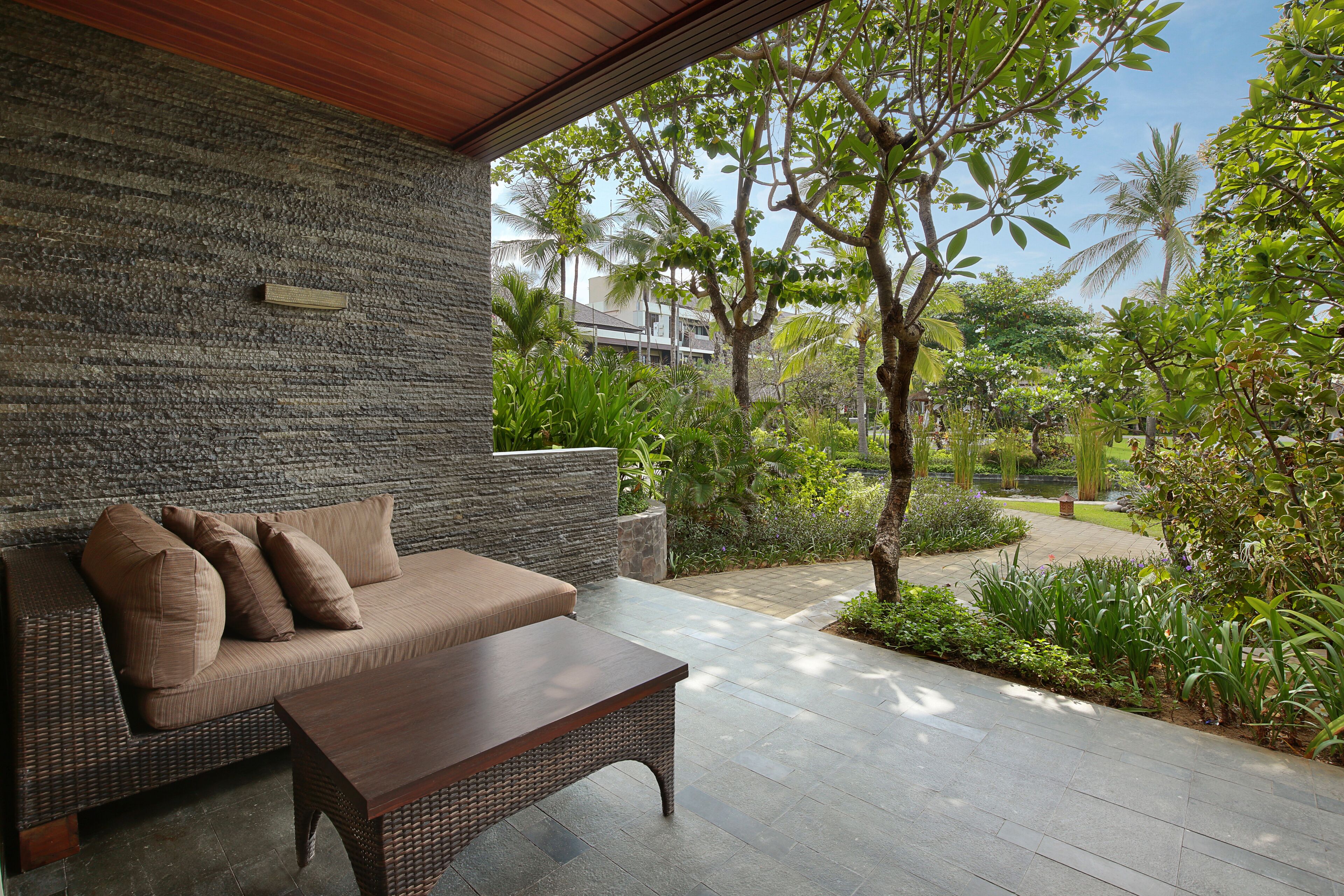 A modern outdoor seating area with a stone wall, a wooden bench, and a cushioned sofa.