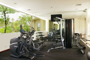 A gym with cardio machines, free weights, and a TV screen.
